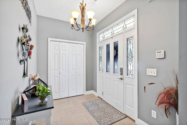 foyer entrance with a chandelier, a textured ceiling, and baseboards