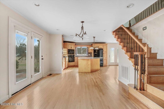 kitchen featuring plenty of natural light, visible vents, a center island, light brown cabinetry, and black appliances