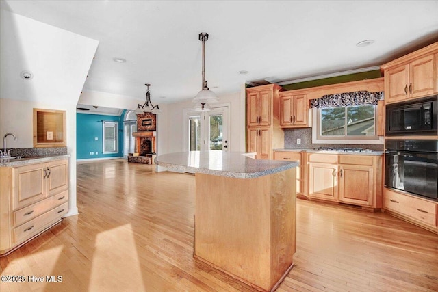 kitchen with a fireplace with raised hearth, a kitchen island, light wood-type flooring, black appliances, and light brown cabinets