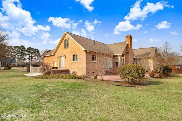 back of house with a lawn, a chimney, crawl space, a patio area, and brick siding