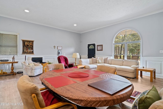 dining area featuring wainscoting, a textured ceiling, crown molding, and light wood-style floors