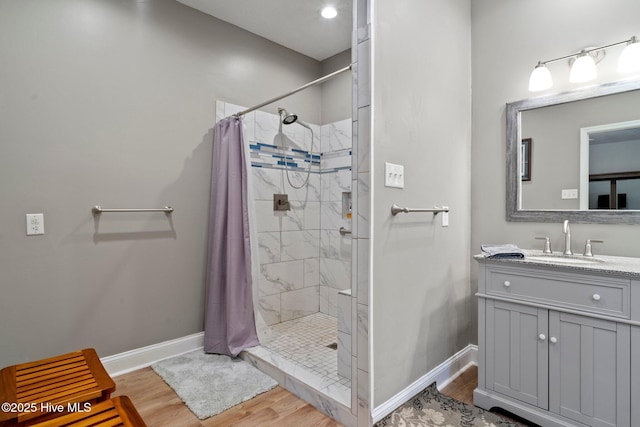 bathroom featuring vanity, wood finished floors, baseboards, and a tile shower