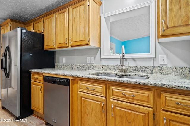 kitchen with light wood-style flooring, a sink, light stone counters, a textured ceiling, and stainless steel appliances