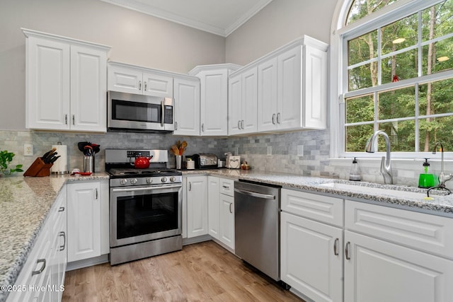 kitchen featuring tasteful backsplash, crown molding, appliances with stainless steel finishes, white cabinetry, and a sink