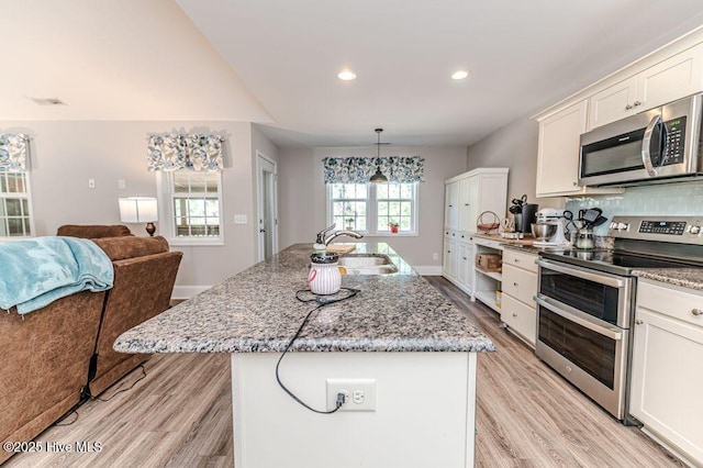 kitchen with light wood finished floors, appliances with stainless steel finishes, light stone countertops, white cabinetry, and a sink