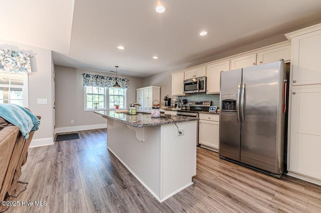 kitchen featuring an island with sink, a breakfast bar, dark stone countertops, wood finished floors, and stainless steel appliances