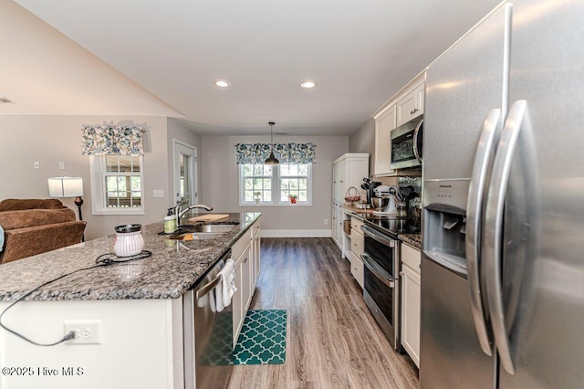 kitchen featuring stone counters, stainless steel appliances, white cabinetry, a sink, and wood finished floors