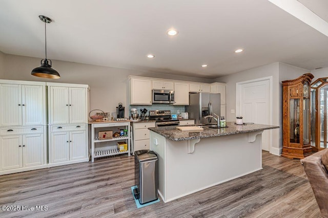 kitchen featuring appliances with stainless steel finishes, a kitchen bar, an island with sink, and wood finished floors