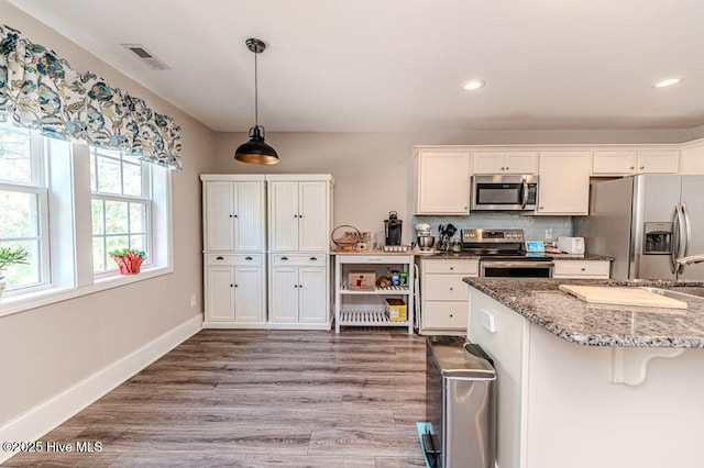 kitchen featuring stainless steel appliances, wood finished floors, white cabinets, and baseboards