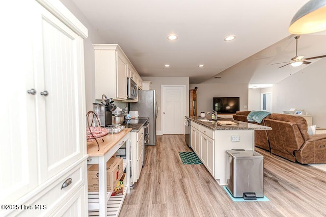 kitchen featuring open floor plan, stainless steel appliances, light wood-type flooring, white cabinetry, and a sink