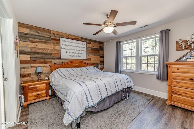 bedroom with wood walls, baseboards, visible vents, and wood finished floors