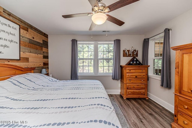 bedroom with wood walls, ceiling fan, baseboards, and dark wood-style flooring