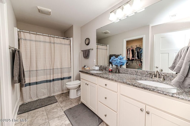 full bath featuring double vanity, a spacious closet, toilet, and a sink