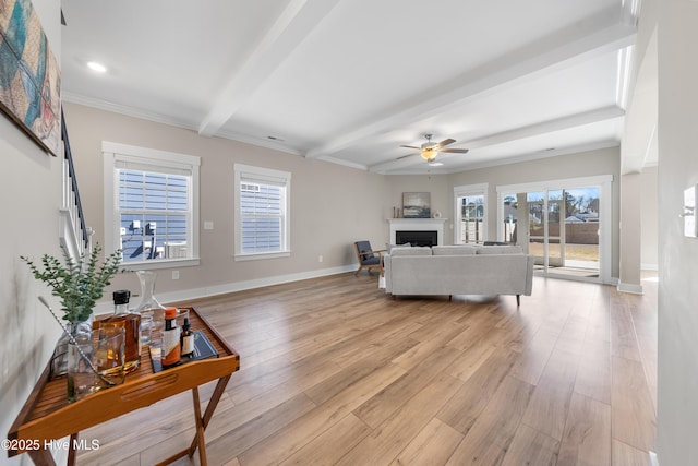 living area featuring plenty of natural light, light wood-type flooring, a fireplace, and beamed ceiling