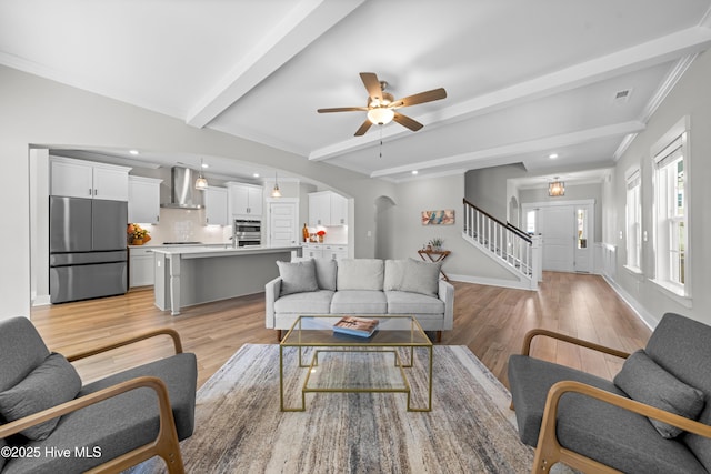 living area featuring arched walkways, beam ceiling, stairway, ornamental molding, and light wood-type flooring