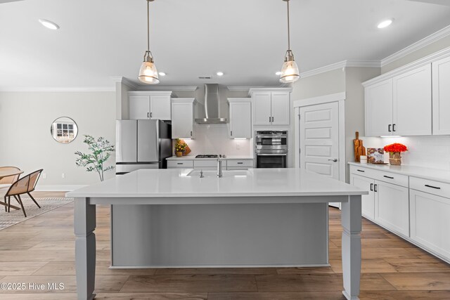 kitchen with wall chimney exhaust hood, light wood-style floors, light countertops, and stainless steel appliances