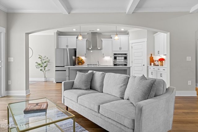 living area featuring light wood-style floors, beamed ceiling, baseboards, and ornamental molding