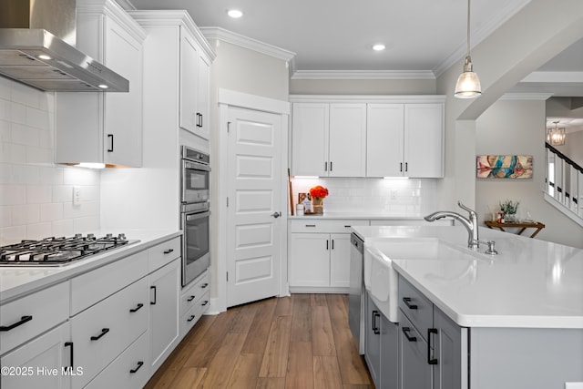 kitchen featuring ornamental molding, wall chimney range hood, appliances with stainless steel finishes, and white cabinets