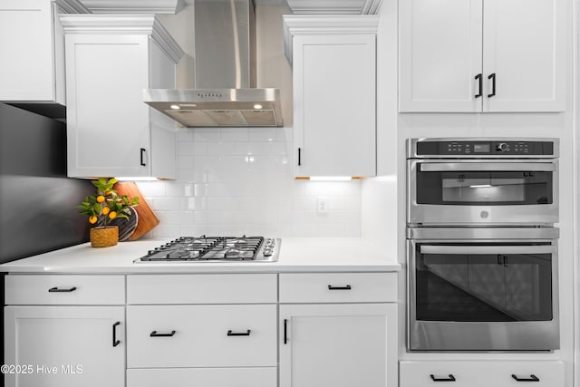 kitchen featuring wall chimney range hood, white cabinetry, stainless steel appliances, and light countertops