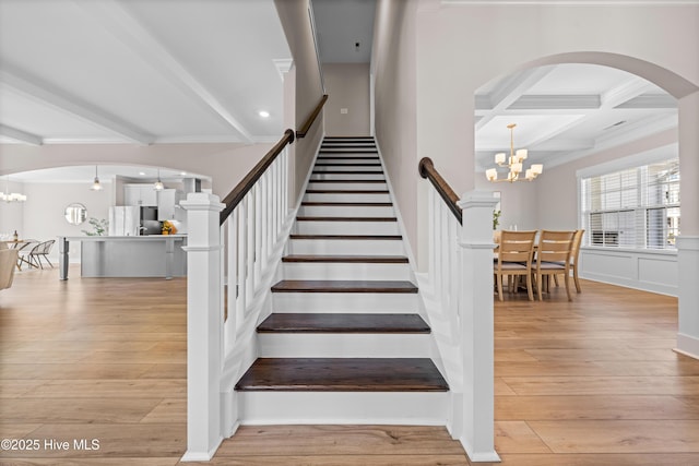 staircase with an inviting chandelier, coffered ceiling, wood finished floors, and beamed ceiling