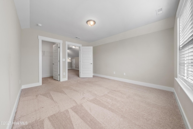 unfurnished bedroom featuring light colored carpet, a walk in closet, visible vents, and baseboards