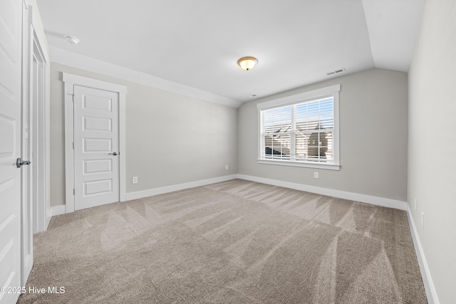 carpeted spare room with visible vents, vaulted ceiling, and baseboards