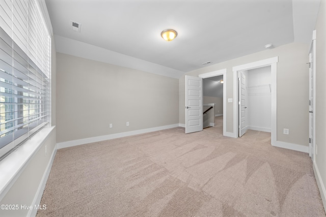 unfurnished bedroom featuring baseboards, visible vents, a walk in closet, and light colored carpet