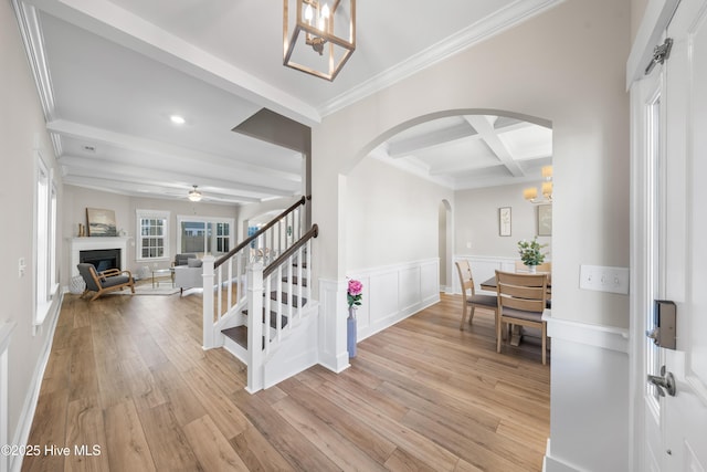 corridor featuring arched walkways, wainscoting, stairway, beamed ceiling, and light wood-type flooring