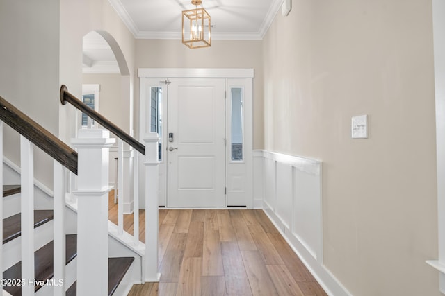 foyer entrance with light wood-type flooring, crown molding, and stairway