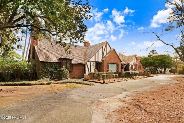 tudor home featuring a chimney and brick siding