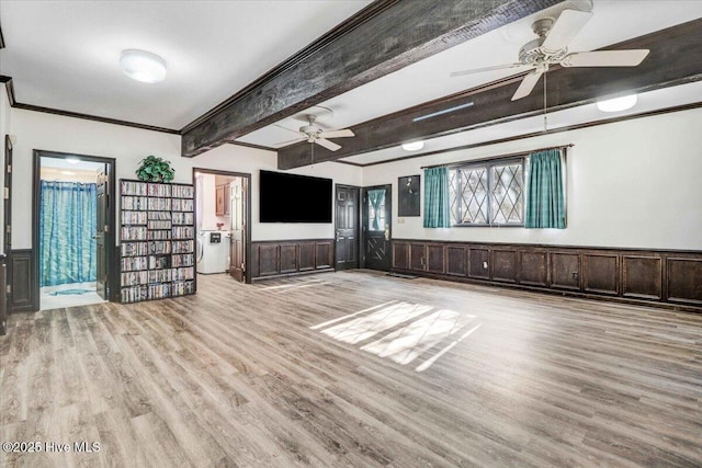 unfurnished living room featuring a ceiling fan, a wainscoted wall, light wood-style flooring, ornamental molding, and beam ceiling