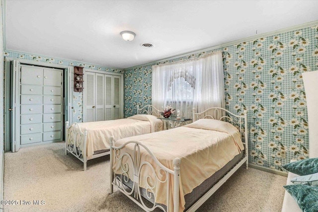 bedroom with wallpapered walls, visible vents, multiple closets, and ornamental molding