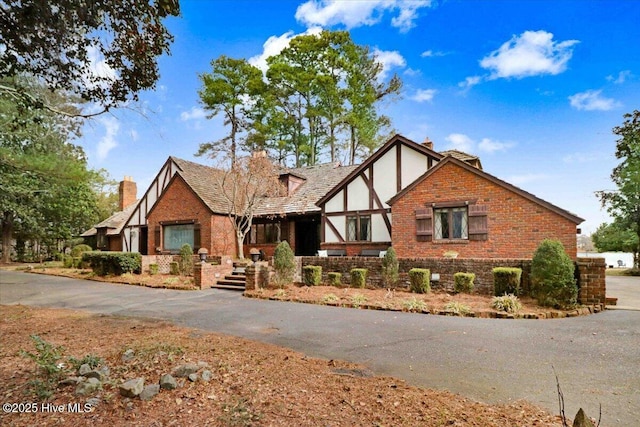 tudor house with brick siding, a chimney, and stucco siding