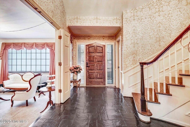 entrance foyer with a wainscoted wall, stone finish floor, stairs, and wallpapered walls