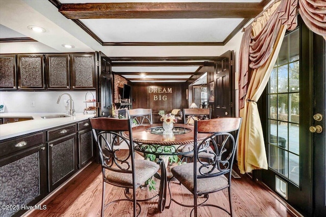 dining space featuring beam ceiling, crown molding, wood walls, and wood finished floors