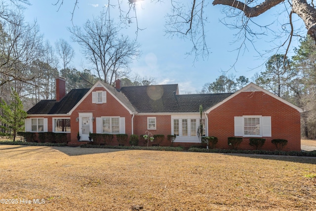 cape cod home with brick siding, a chimney, and a front lawn