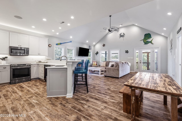 kitchen with appliances with stainless steel finishes, open floor plan, a kitchen breakfast bar, a peninsula, and light countertops