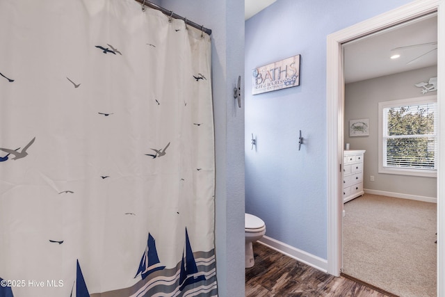 bathroom with curtained shower, wood finished floors, toilet, and baseboards