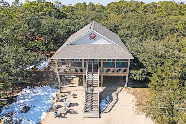 view of front of house featuring a shingled roof, stairway, a sunroom, and a view of trees