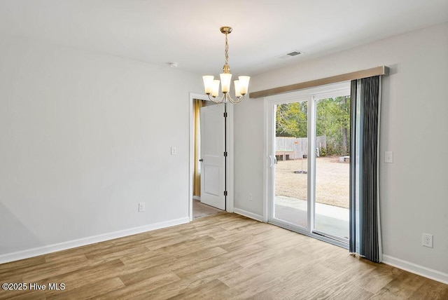 spare room featuring an inviting chandelier, visible vents, baseboards, and wood finished floors