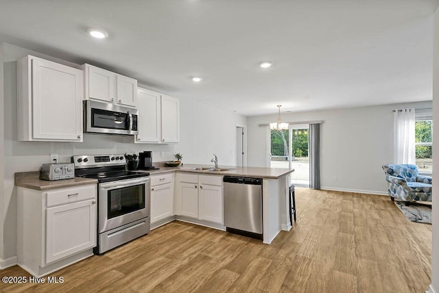 kitchen with stainless steel appliances, a peninsula, a sink, white cabinets, and light wood finished floors