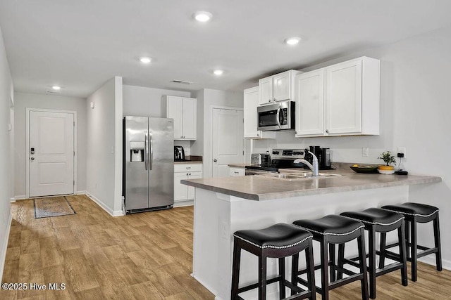 kitchen with light wood finished floors, appliances with stainless steel finishes, a peninsula, a kitchen bar, and a sink