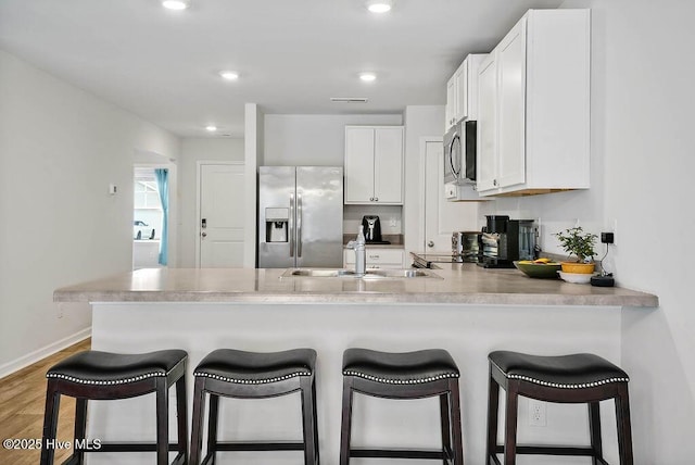 kitchen with a peninsula, stainless steel appliances, light wood-type flooring, white cabinetry, and a sink