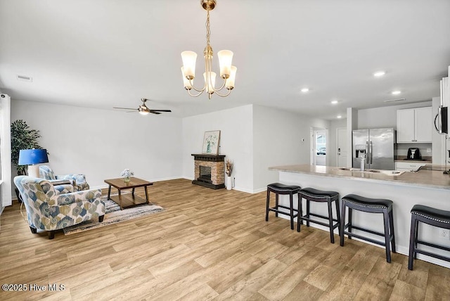 kitchen with a fireplace with raised hearth, appliances with stainless steel finishes, light wood-style floors, and a kitchen breakfast bar