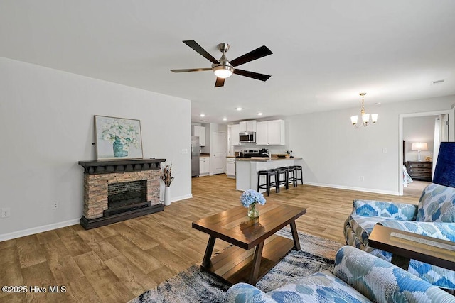 living area with light wood-style flooring, a fireplace, baseboards, and ceiling fan with notable chandelier