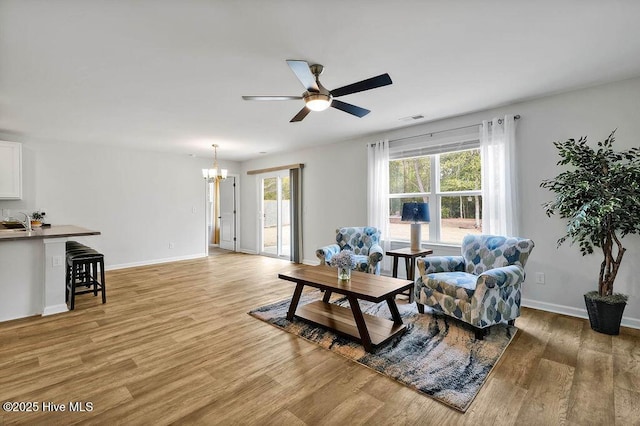 living room featuring ceiling fan with notable chandelier, light wood finished floors, visible vents, and baseboards