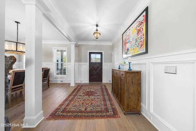 foyer entrance featuring a notable chandelier, crown molding, ornate columns, and hardwood / wood-style floors