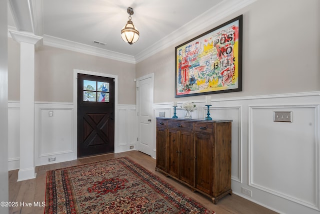 foyer entrance featuring visible vents, ornamental molding, wainscoting, light wood finished floors, and ornate columns