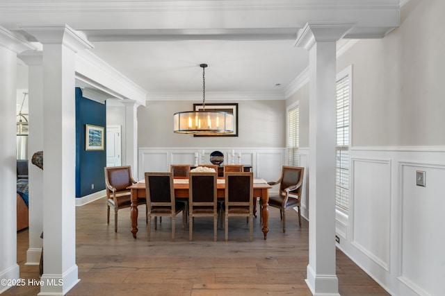 dining room featuring a decorative wall, wood-type flooring, ornate columns, and ornamental molding