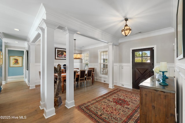 entryway with decorative columns, ornamental molding, wood-type flooring, wainscoting, and a decorative wall